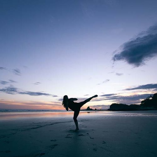 IV Drips Can Improve Wellness silhouette of a woman doing a high kick on the beach at sunset