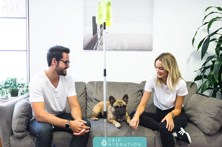 Drip Hydration - Mobile IV Therapy - Hawaii Man and woman getting IV in her home on their couch, their dog is with them