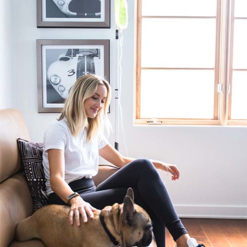 In Home NAD IV Therapy--- A woman getting a vitamin IV therapy at her home while she is petting her small dog.