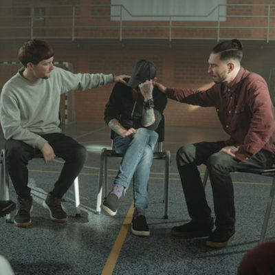 group-counseling-addiction two people consoling a man in a gym during an anonymous meeting for addicts